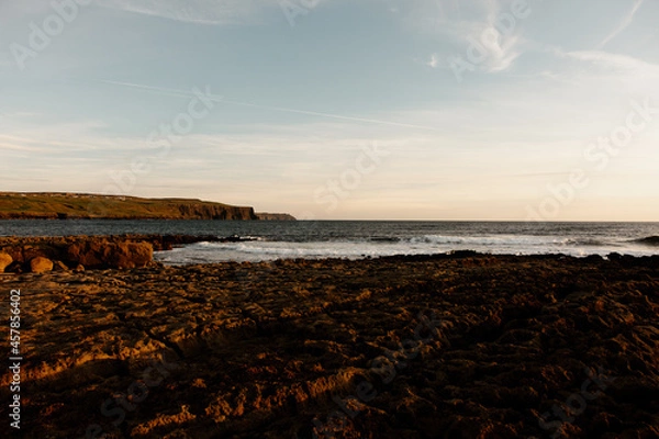 Fototapeta Sunset on a rocky beach in Ireland. Beautiful earth and warm tones on the image. Harsh shadows on the rocks. Summer outdoor sunset on the Atlantic Ocean. 