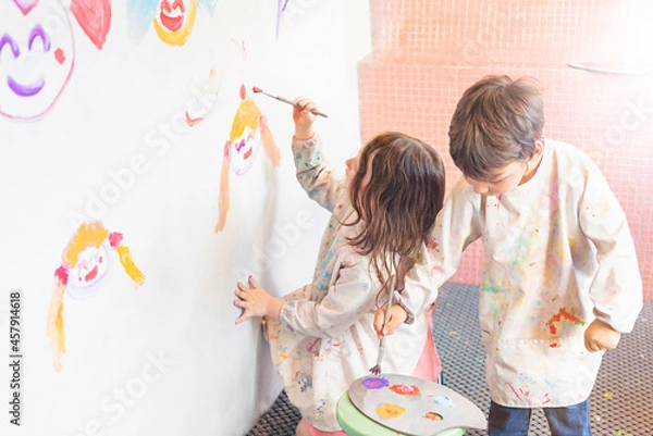 Obraz Little kids draws with paints on a white wall, back view