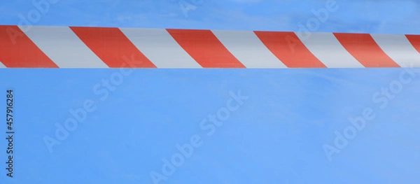 Fototapeta Signal red-white tape on a blue background. Red And White Warning Tape On A Blue.