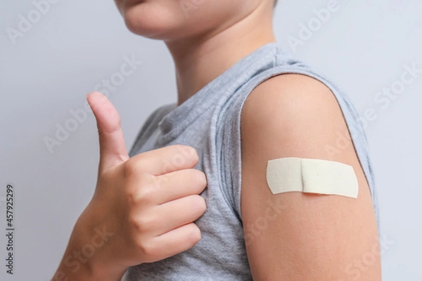 Fototapeta An arm of a boy with adhesive bandage plaster on it after vaccination showing thumb up, injection covid vaccine, healthcare for children and teenagers