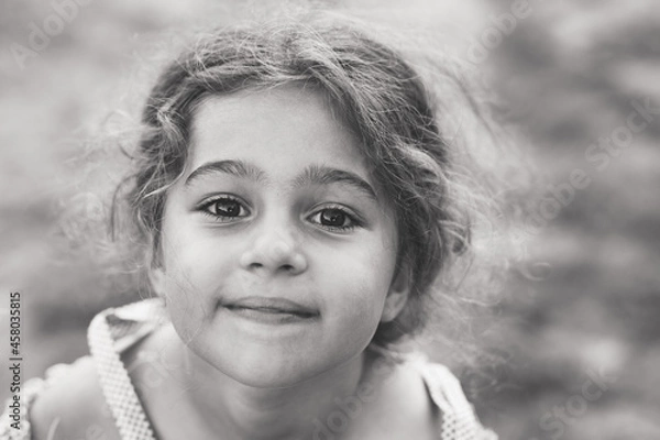 Obraz Black and white Portrait of smiling cute little girl at summer park. Happy child looking at the camera