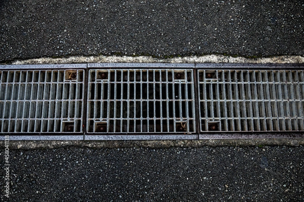 Obraz アスファルトの道路を横切る側溝のグレーチング
