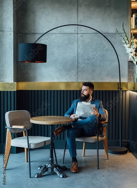 Fototapeta Handsome Businessman Reading Newspaper in a Cafe.
 
Serious elegant business man with a newspaper sitting in a restaurant and looking away. 