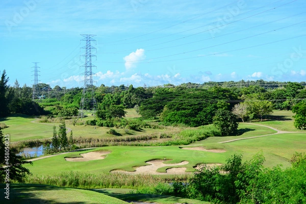 Fototapeta View of Golf Course with putting green, green grass, sand bunker, blue sky, and high voltage electric transmission tower background. Using for Golf field banner with a copy for your text.