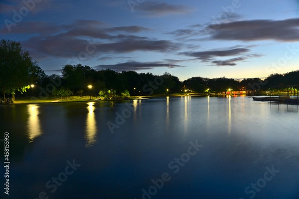 Fototapeta A long exposure of Beaver Lake, Mount Royal, Montreal, QC, Canada at twilight blue hour on a cloudy summer day. The lights and trees reflect on the lake.