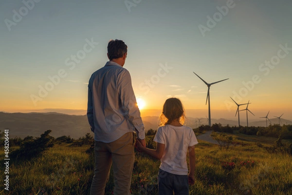 Obraz Cinematic shot of carefree young father engineer keeping his daughter for hand and looking on windmill field at sunset. Concept of renewable energy, love for nature, family, electricity, green, future
