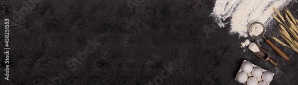 Fototapeta The banner. Baking background with free space for your text. Flour in a bowl, eggs and wheat on a black table