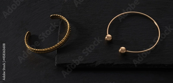 Fototapeta Top view of Two modern gold braid shape bracelets on black stone trays