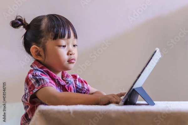 Fototapeta Portrait image of 3-4 years old preschool kid. Bored Asian child girl using and touching smart pad or tablet for do her homework and online learning (E-learning). Back to school, Study from home.