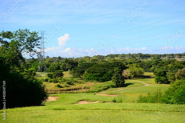 Fototapeta View of Golf Course with putting green, green grass, sand bunker, blue sky, and high voltage electric transmission tower background. Using for Golf field banner with a copy for your text.