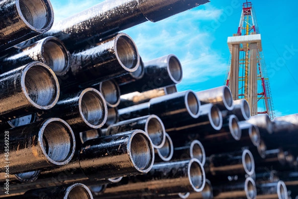 Fototapeta In the foreground pipes for drilling oil and gas wells. In the background, a blurred image of the rig out of focus. Blue sky with clouds.