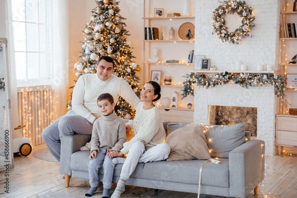 Fototapeta Happy beautiful family with a small son sitting on the couch in the house on the background of the Christmas tree