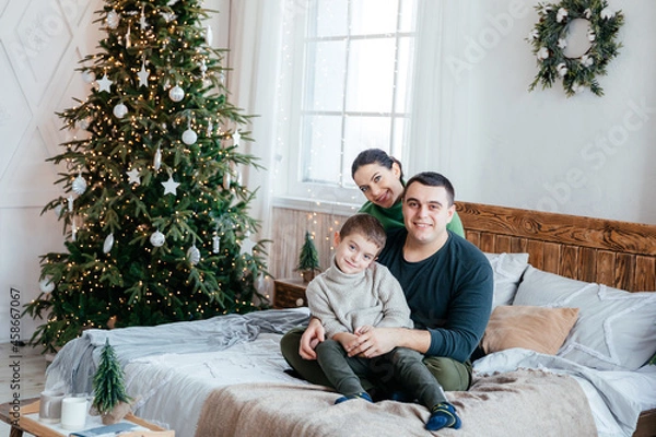 Fototapeta Happy beautiful family with a small son sitting on the couch in the house on the background of the Christmas tree
