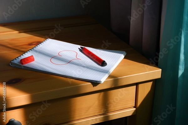 Fototapeta Drawing of a heart in a notebook. The sun's rays fall on the table and notebook. Valentine's Day.