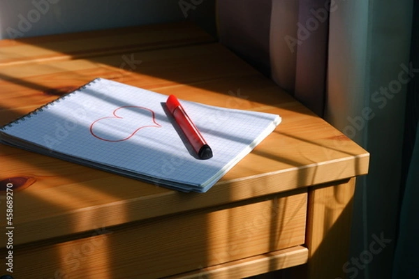 Fototapeta Drawing of a heart in a notebook. The sun's rays fall on the table and notebook. Valentine's Day.