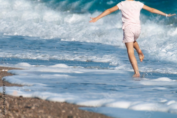 Fototapeta a child runs along the seashore among the waves on a clear day