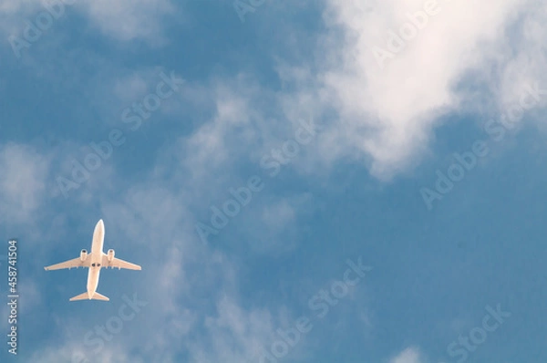Fototapeta white passenger plane flies against the background of a bright blue sky with clouds