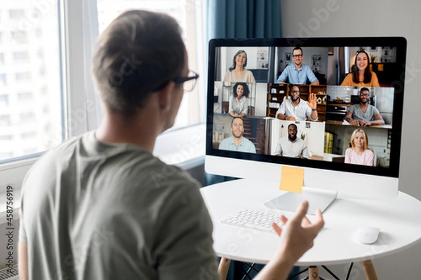 Fototapeta View from back above male shoulder on the laptop with diverse employees, coworkers on the screen, video call, online meeting. App for video conference with many people together