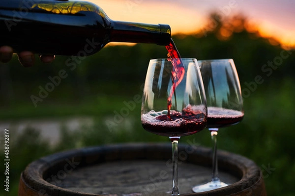 Obraz Pouring red wine into glasses on the barrel at dusk