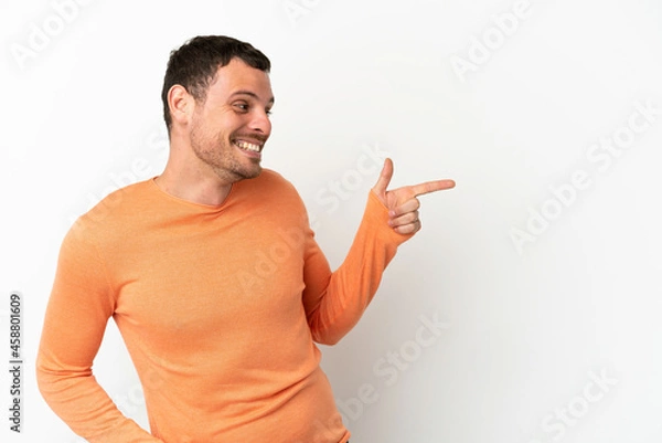 Fototapeta Brazilian man over isolated white background pointing finger to the side and presenting a product