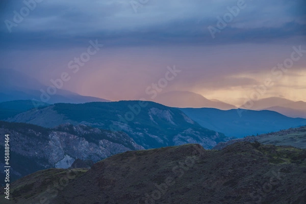 Fototapeta Atmospheric landscape with silhouettes of mountains with trees on background of vivid orange blue lilac dawn sky. Colorful nature scenery with sunset or sunrise of illuminating color. Sundown paysage