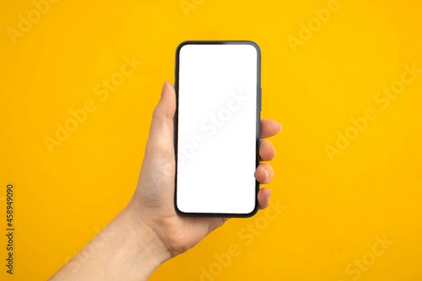 Obraz Person holding mobile phone with blank white screen on a yellow background, copy space photo