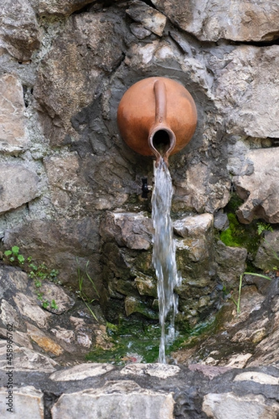 Obraz Decorative garden waterfall water flows from a decorative jug.