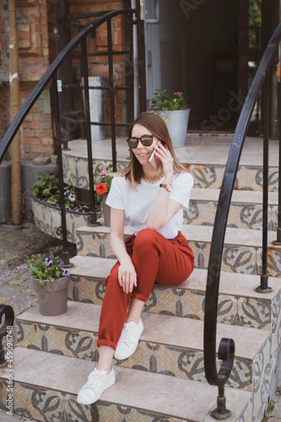 Obraz Stylish woman sitting on the steps of a building on the street and talking on the phone