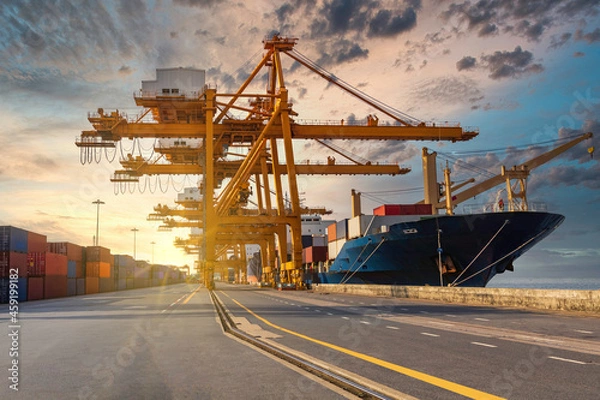 Obraz Container loading in a cargo freight ship with crane to shore lift up loading during cargo operation in sunrise time import and export  logistic and transportation concept.