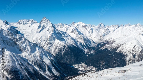 Fototapeta Caucasus Mountains, Panoramic view of the ski slope with the mountains Belalakaya, Sofrudzhu and Sulakhat on the horizon in winter day. Dombai ski resort, Western Caucasus, Karachai-Cherkess, Russia.