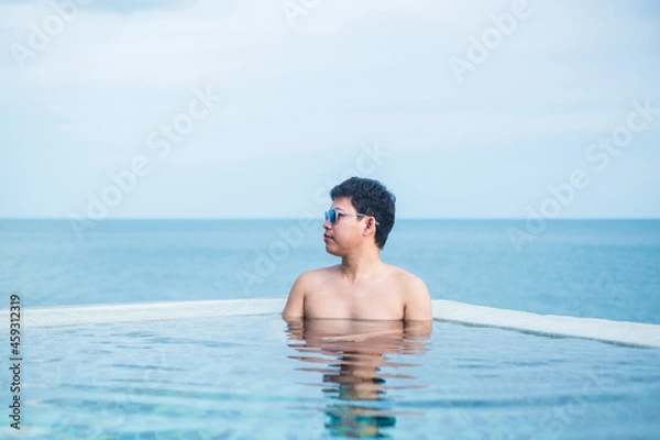 Obraz Happy man in infinity pool at luxury hotel against ocean front. young male enjoy in tropical resort. Relaxing, summer,  travel, holiday, vacation and weekend concept