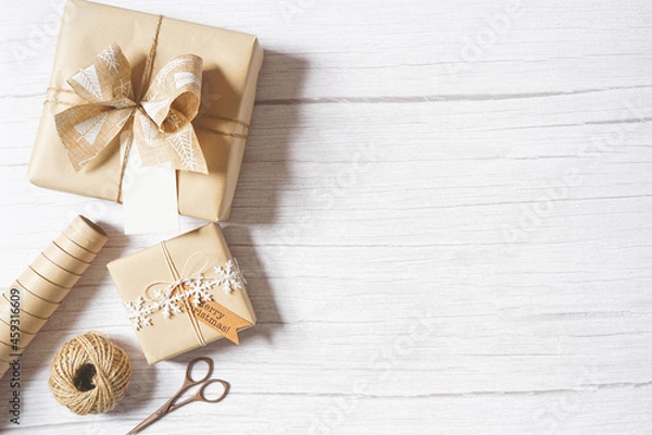 Fototapeta Christmas composition with decoration, presents, scissors, natural paper, twine on white wooden background. Holiday craft gift wrapping. Merry Christmas greetings. Empty space for text. Copy space.