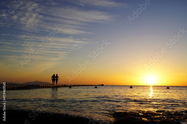 Obraz Colorful sunset by the ocean, two people walk across the bridge, two silhouettes             
