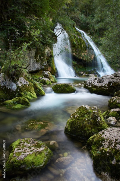 Fototapeta Long exposure of a beautiful waterfall in Slovenia. Small stream with mossy rocks and a beautiful waterfall in the background..