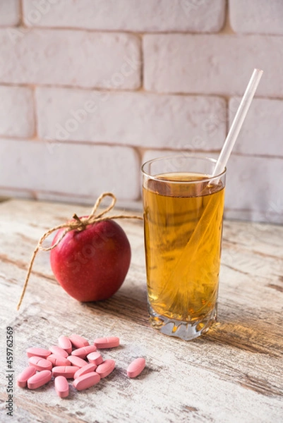 Fototapeta Scattered pills, glass of fresh juice with straw and an apple. Choice of healthy life. Vertical photo