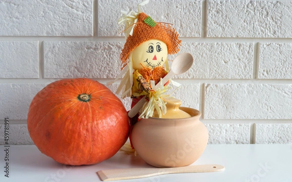 Fototapeta A scarecrow with a wooden spoon,a clay pot and a pumpkin on a white background.Halloween and Thanksgiving Day Concept