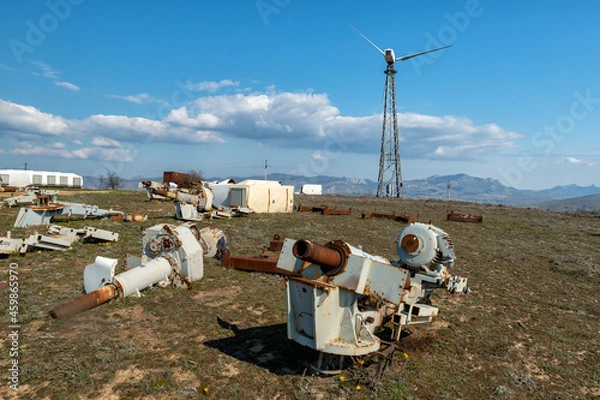 Obraz An abandoned wind power station with one wind turbine and rusty spare parts in the foreground.