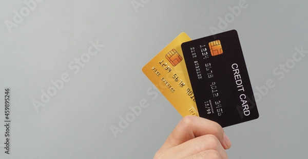 Fototapeta Hand is holding two credit card in black and gold color isolated on grey background..