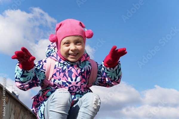 Obraz Funny little girl on a background of blue sky. Scares people. Pink clothes. Child laughing in the street.