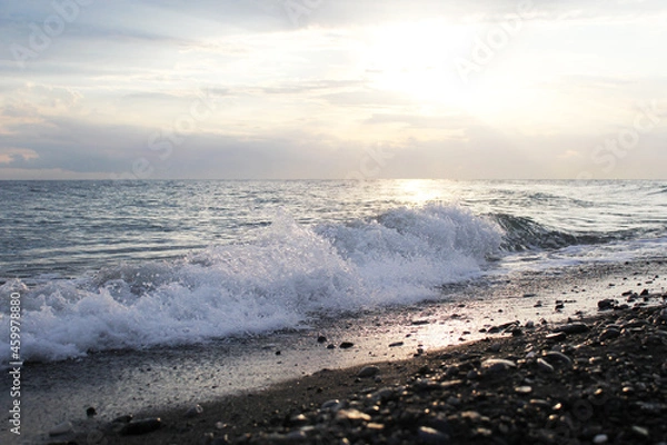 Fototapeta Sunset on the seashore. The sun shines through the white sea foam. An empty beach. Calm sea at sunset. The concept of privacy and relaxation.