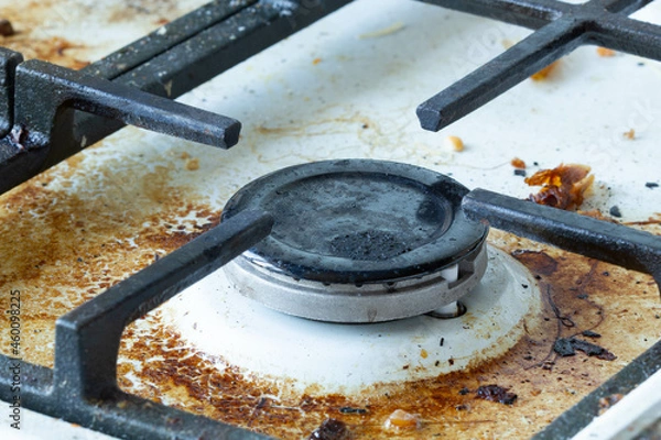 Fototapeta Dirty gas stove surface. Medium gas burner and cast iron grate of a gas oven surrounded by old leftovers of food and drinks. Top area surface and burner heads needs cleaning from burnt-on grease