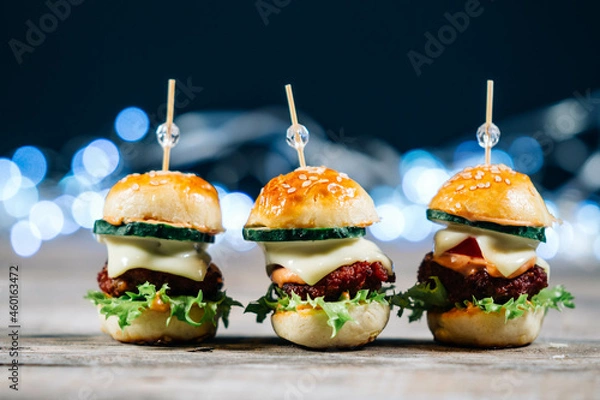 Fototapeta Close up of mini burgers with cheese, onion, lettuce salad and cucumber, isolated on wood background. Party snacks, fast food concept