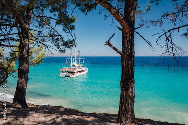 Fototapeta Blue sea on the Turkish coast. A boat with tourists stands near the shore. People swim in azure water. Dilek National Park, Kusadasi, Turkey