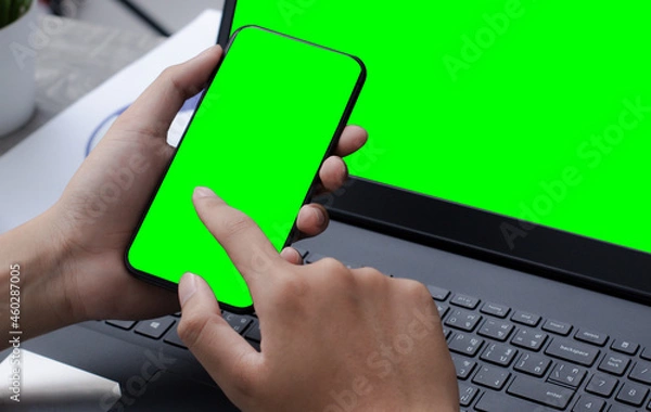 Obraz mobile phone laptop with blank green screen on desk.