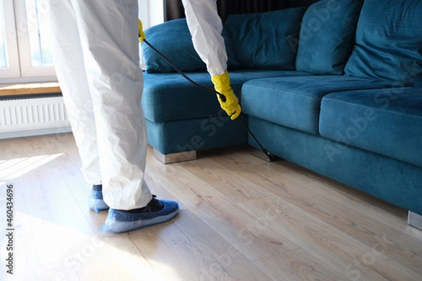 Fototapeta Person in protective suit and gloves is treating room from painful bacteria. Disinfection of premises concept