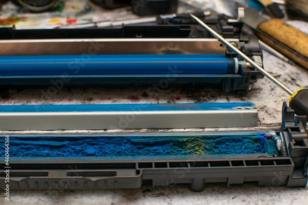 Fototapeta a view of colored toner in the hopper of the blue laser printer cartridge, which lies against the background of the disassembled unit next to a screwdriver, tools on the service work table