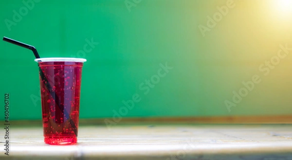 Obraz Red water in a plastic glass has a sucker tube, has a background and is sunny.