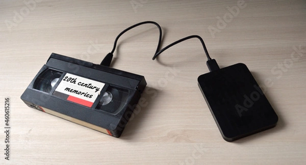 Fototapeta A video tape labeled  as '20th century memories' plugged to a hard disk drive as a symbol of data transfer from analog to digital.