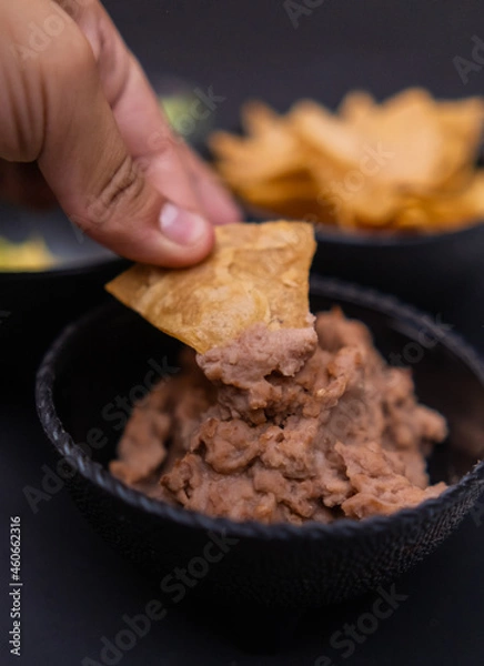Fototapeta Hand dipping tortilla chip in bowl of refried beans