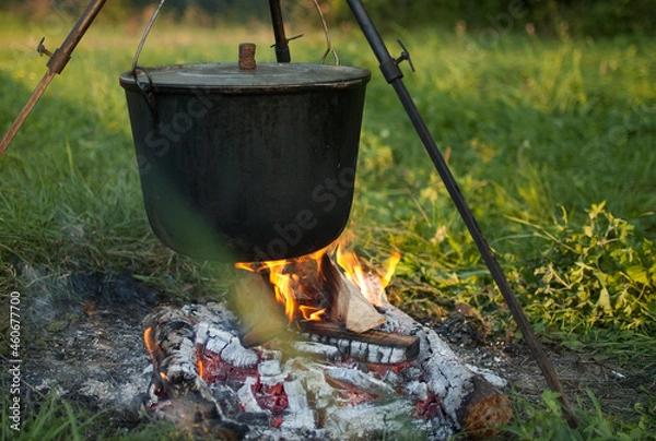 Fototapeta Dark big pot or cauldron, cooking pan with boiling water inside above the fire somewhere in the park or mountains, camping concept